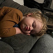 Ryan is registered to the contest to win money with this photo: toddler, sleeping, child, couch, sofa, brown_clothing, blonde_hair, indoor, cozy, resting, peaceful, home, furniture, blanket, portrait, young_child, relaxation, curly_hair, face, comfort