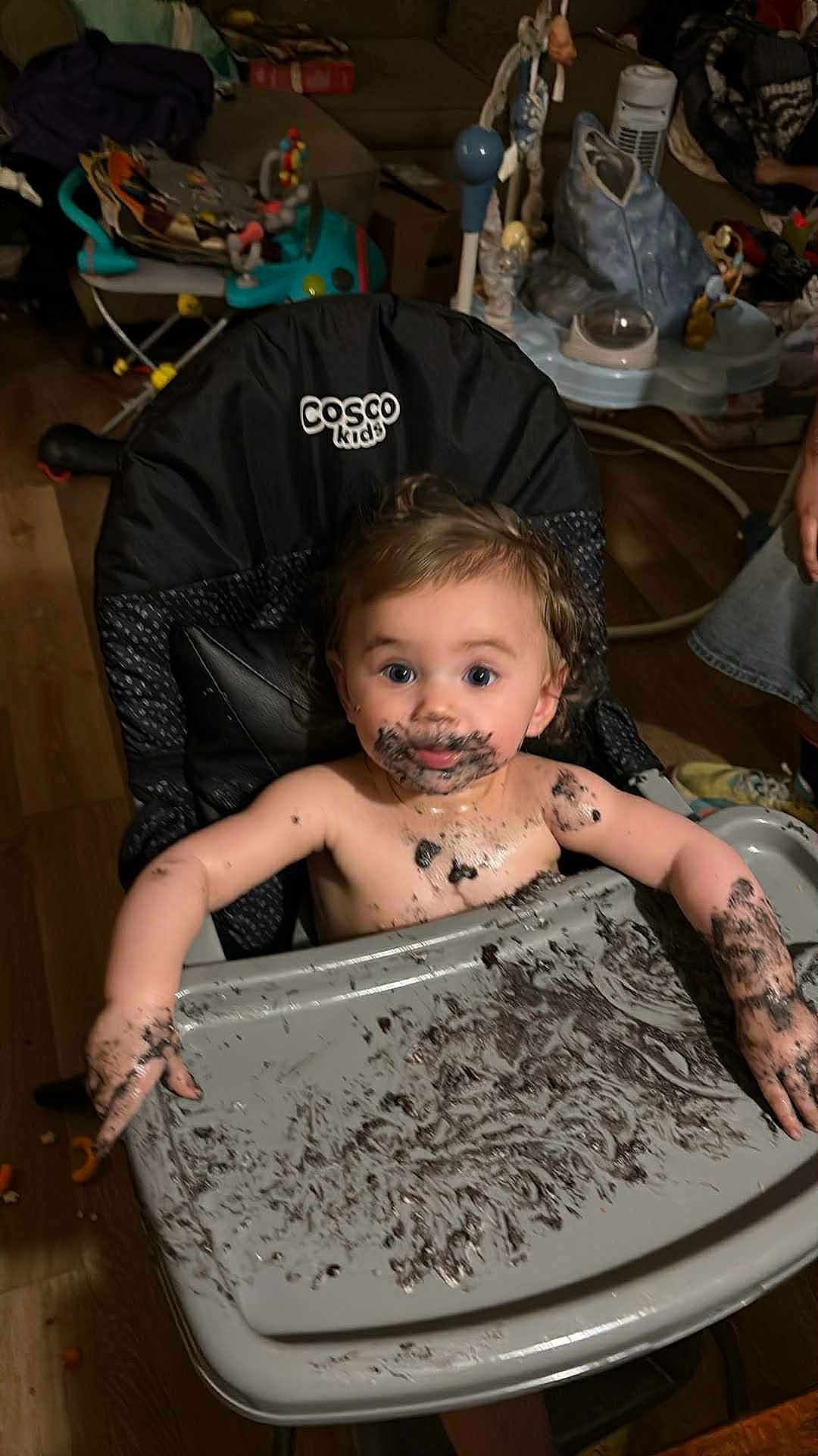 Marilyn is registered to the contest to win money with this photo: baby, child, high_chair, messy, chocolate, food, face_paint, arms, tray, indoor, wooden_floor, couch, toy, person, smudged, curly_hair, blue_eyes, expression, mess, cosco_kids