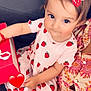 child, colorful, curious_eyes, cute, dress, fabric, girl, hair_clip, heart_emoji, holding, indoor, patterned_clothing, person, portrait, red_box, sitting, smiling, strawberry, toddler, young_child