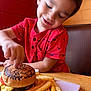 booth, boy, burger, casual_dining, cheese, child, cute, fast_food, food, fries, happy, indoor, meal, red_shirt, restaurant, shark_print, smiling, table, tomato, wooden_table