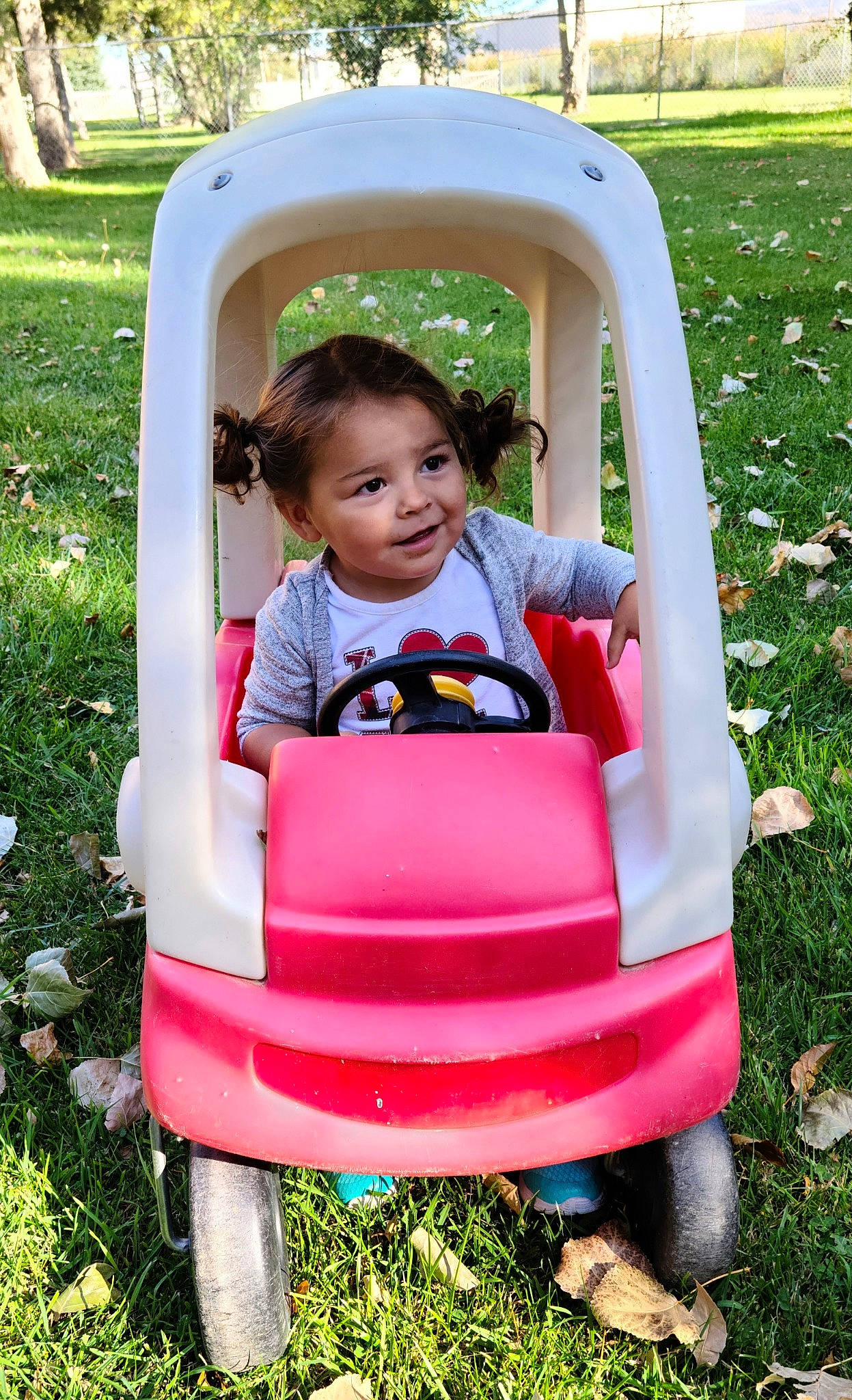 Tynnessee is registered to the contest to win money with this photo: baby_toddler_clothing, comfort, face, grass, green, happy, head, leisure, motor_vehicle, people_in_nature, person, pink, plant, public_space, recreation, riding_toy, tire, toddler, tree, vehicle
