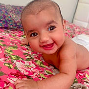 Zahra joined the competition — help win amazing prizes! baby, child, smiling, happy, face, skin, bedspread, floral, pattern, pink, green, hand, arm, lying, indoor, infant, cute, portrait, person, head