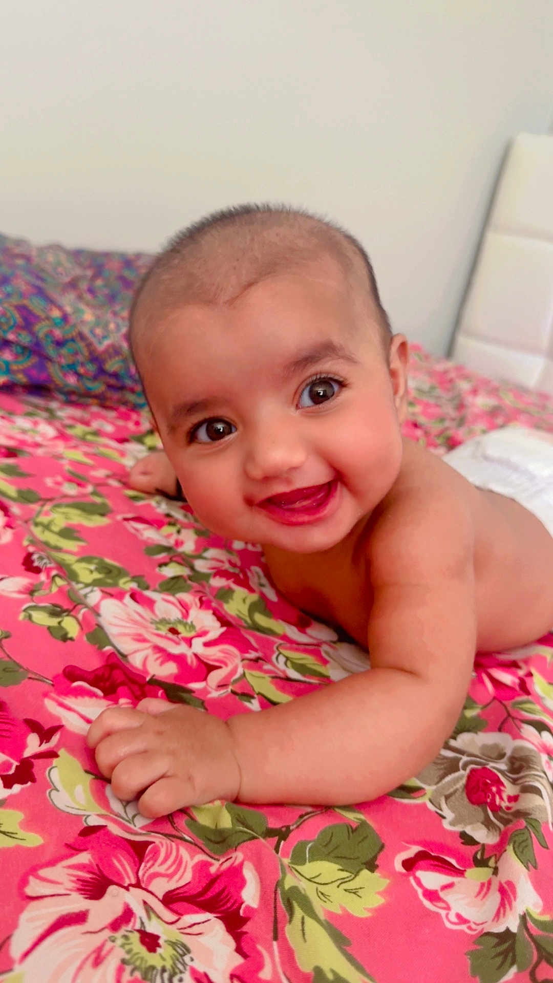 Zahra joined the competition — help win amazing prizes! baby, child, smiling, happy, face, skin, bedspread, floral, pattern, pink, green, hand, arm, lying, indoor, infant, cute, portrait, person, head