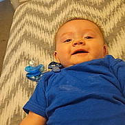 Austin Pierce joined the competition — help win amazing prizes! baby, blue_shirt, pacifier, blanket, smiling, lying_down, infant, child, bedroom, furniture, drawer, carpet, clip, happy, face, person, indoors, young_child, pattern, fabric