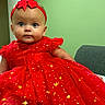 baby, child, infant, portrait, red_dress, hair_bow, headband, sparkly_dress, formalwear, sitting, face, eyes, looking_at_camera, indoor, chair, green_wall, fashion, cute, colorful, photography