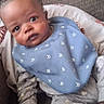 baby, infant, child, portrait, face, wide_eyed, sitting, couch, sofa, cushion, bib, blue_clothing, bottle, baby_bottle, indoor, home, furniture, patterned_blanket, close_up, photography