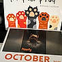 2025, animal, calendar, cartoon, cover, cute, dark_background, decor, dog, floofy, illustration, october, paper, paw_print, pet, photograph, small_dog, spiral_binding, table, text
