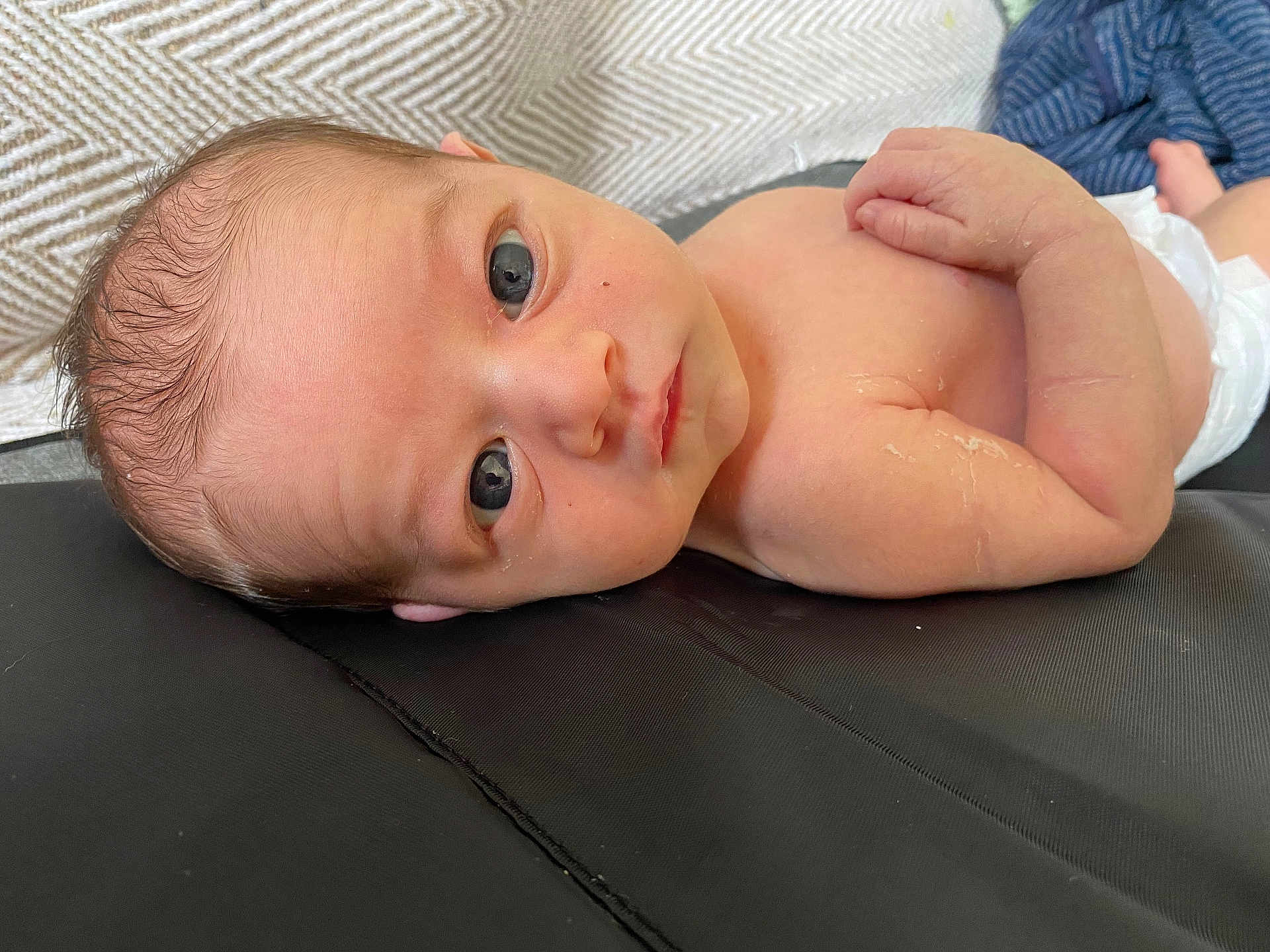 Noah joined the competition — help win amazing prizes! baby, newborn, infant, skin, diaper, face, eyes, hand, fingers, lying_down, curious, peeling_skin, black_surface, texture, closeup, portrait, human, child, small, cute