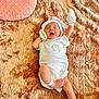 newborn, baby, infant, white_clothing, mittens, hat, blanket, pink_cushion, heart_shaped, yawning, sleepy, hospital_band, soft_texture, lying_down, cute, small, resting, indoors, comfort, peaceful