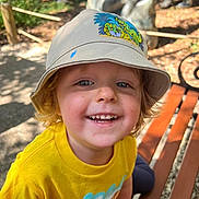 Axton joined the competition — help win amazing prizes! child, smiling, hat, bucket_hat, yellow_shirt, outdoor, bench, dirt, happy, portrait, daylight, cute, face, young, casual_clothing, nature, sunlight, blond_hair, playful, dinosaur_print