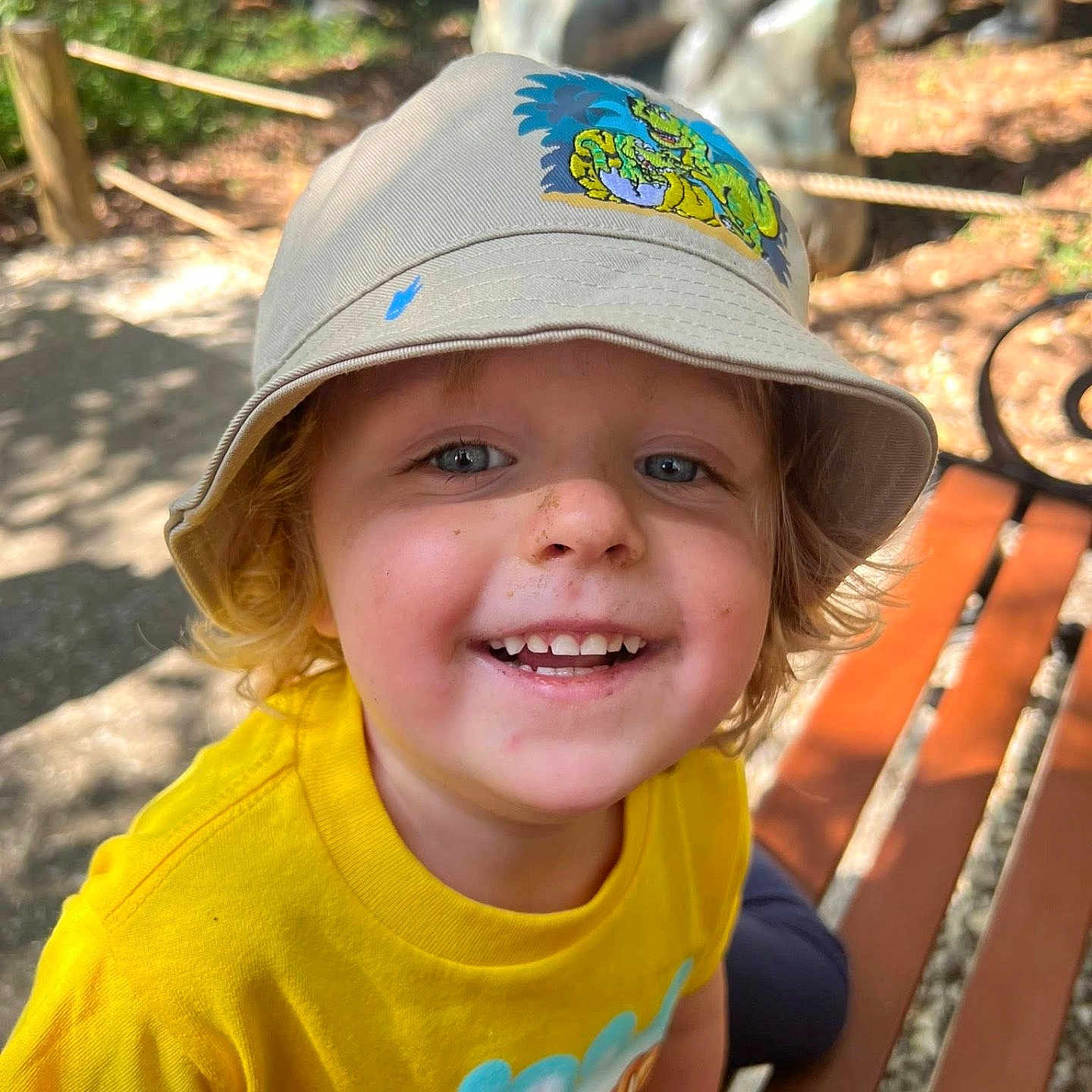 Axton joined the competition — help win amazing prizes! bench, blond_hair, bucket_hat, casual_clothing, child, cute, daylight, dinosaur_print, dirt, face, happy, hat, nature, outdoor, playful, portrait, smiling, sunlight, yellow_shirt, young