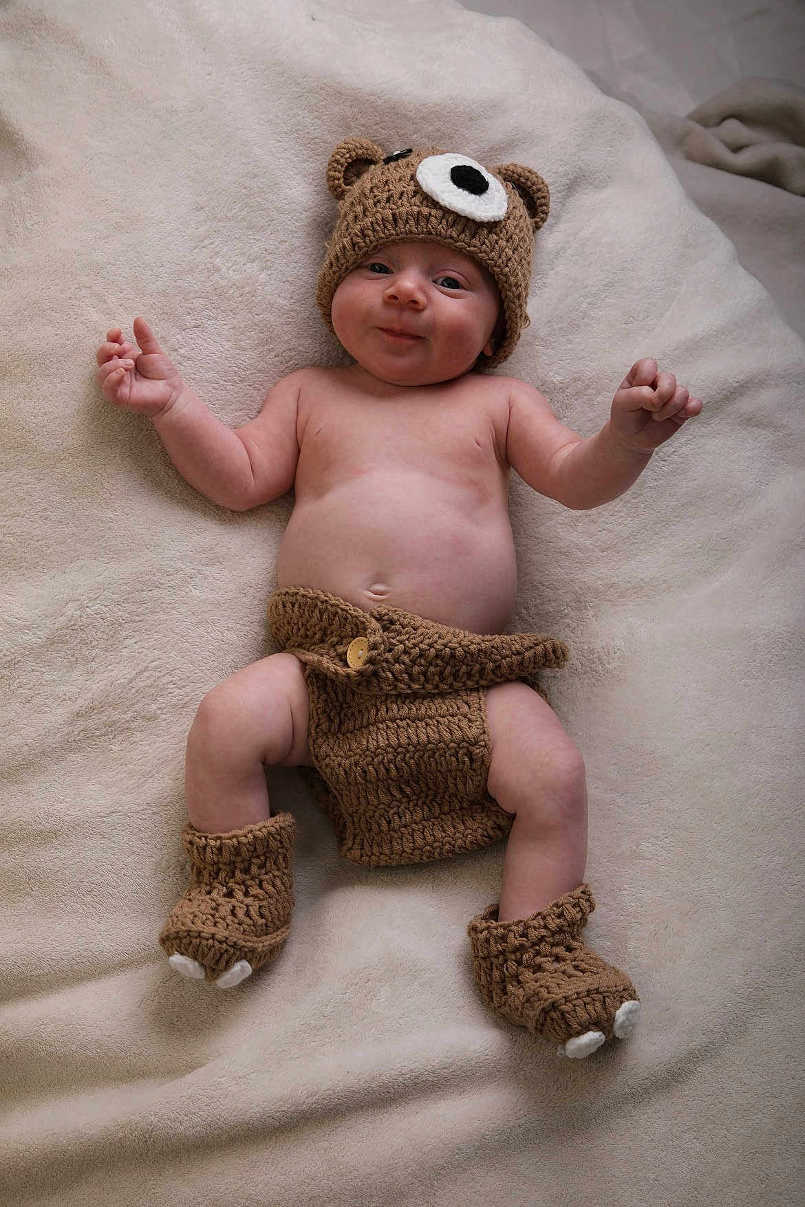 Charlie is registered to the contest to win money with this photo: baby, infant, crocheted_clothing, bear_hat, booties, diaper_cover, smile, lying_down, blanket, cute, cheeks, soft_texture, headwear, hand, footwear, skin, child, young, adorable, warm
