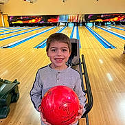 Théo participe au concours pour gagner de l'argent avec cette photo : activity, bowling_alley, bowling_ball, boy, casual_clothing, child, entertainment, fun, game, happy, holding, indoor, lanes, leisure, person, recreation, short_hair, smile, sport, young
