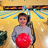 activity, bowling_alley, bowling_ball, boy, casual_clothing, child, entertainment, fun, game, happy, holding, indoor, lanes, leisure, person, recreation, short_hair, smile, sport, young