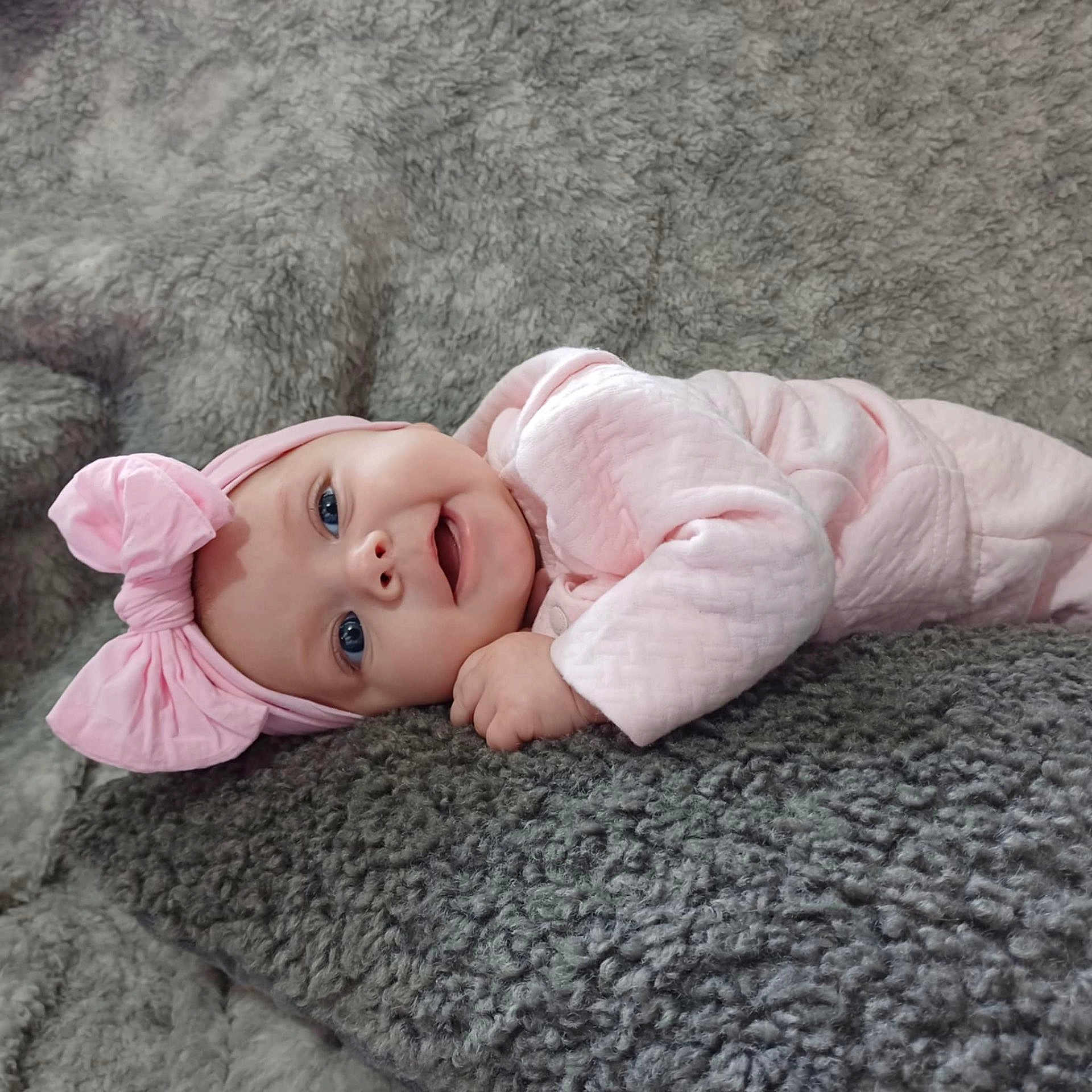 Khalayah is registered to the contest to win money with this photo: baby, infant, pink_bow, headband, smiling, lying_down, blanket, soft_texture, cute, child, portrait, happy, cozy, indoors, clothing, pink_outfit, face, small_hand, blue_eyes, toddler