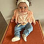 Cassie Anna June participe au concours pour gagner de l'argent avec cette photo : baby, child, headband, curly_hair, cardigan, floral_top, jeans, shoe, orange_bedspread, wooden_frame, indoor, portrait, cute, sitting, smiling, person, floor, wall, clothing, infant