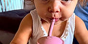 Cassie Anna June participe au concours pour gagner de l'argent avec cette photo : toddler, child, curly_hair, pink_cup, straw, white_tank_top, bracelet, indoor, table, wooden_table, close_up, face, big_eyes, drinking, cute, person, young_child, casual, focused, curious