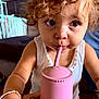 toddler, child, curly_hair, pink_cup, straw, white_tank_top, bracelet, indoor, table, wooden_table, close_up, face, big_eyes, drinking, cute, person, young_child, casual, focused, curious