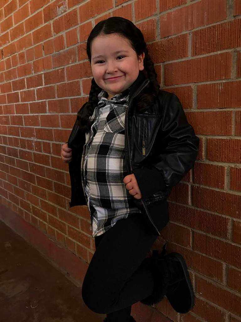 Aryanna is registered to the contest to win money with this photo: brick, child, child_model, design, fun, jacket, joy, outerwear, pattern, person, photography, plaid, smile, snapshot, standing, style, tartan, textile, wall, winter