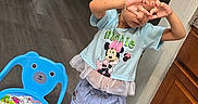 Linda joined the competition — help win amazing prizes! blue_shirt, cabinet, cartoon, child, cute, floor, footwear, girl, hair_clip, hands, heart_shape, home, indoor, minnie_mouse, person, playful_pose, shorts, slippers, toy_chair, wooden_cabinet