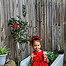 Linda is registered to the contest to win money with this photo: child, girl, red_dress, bow, smiling, drink_can, plant, flower, potted_plant, garden, wooden_fence, outdoor, greenery, happy, playful, standing, nature, casual, daytime, cute