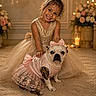 child, girl, smiling, dog, french_bulldog, dress, pink, gold, bow, flower_arrangement, carpet, candle, indoor, portrait, cute, pet, happy, elegant, warm_lighting, celebration