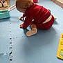 activity, baby, blue_mat, child, corner, crawling, curly_hair, floor, indoor, light, plastic_container, play_area, puzzle, red_clothing, shoes, toddler, toys, wall, white_socks, wooden_floor
