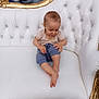 baby, balloons, barefoot, casual_clothing, child, couch, curious, cute, decor, gold_trim, gray_balloons, indoor, luxury, pants, portrait, short_sleeve_shirt, sitting, smiling, toddler, white_couch