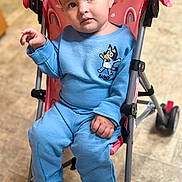 Sophia is registered to the contest to win money with this photo: toddler, child, stroller, blue_clothing, indoor, floor, pink, rainbow_pattern, sitting, curious_expression, person, footwear, toy_character, casual_wear, baby, young_child, face, hand, legs, wheel