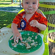 Liam is registered to the contest to win money with this photo: birthday, cake, celebration, child, clothing, colorful, face_paint, fun, grass, green_plate, happy, high_chair, messy, outdoor, party, red_hair, smiling, sunlight, toddler, tree