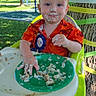 birthday, cake, celebration, child, clothing, colorful, face_paint, fun, grass, green_plate, happy, high_chair, messy, outdoor, party, red_hair, smiling, sunlight, toddler, tree