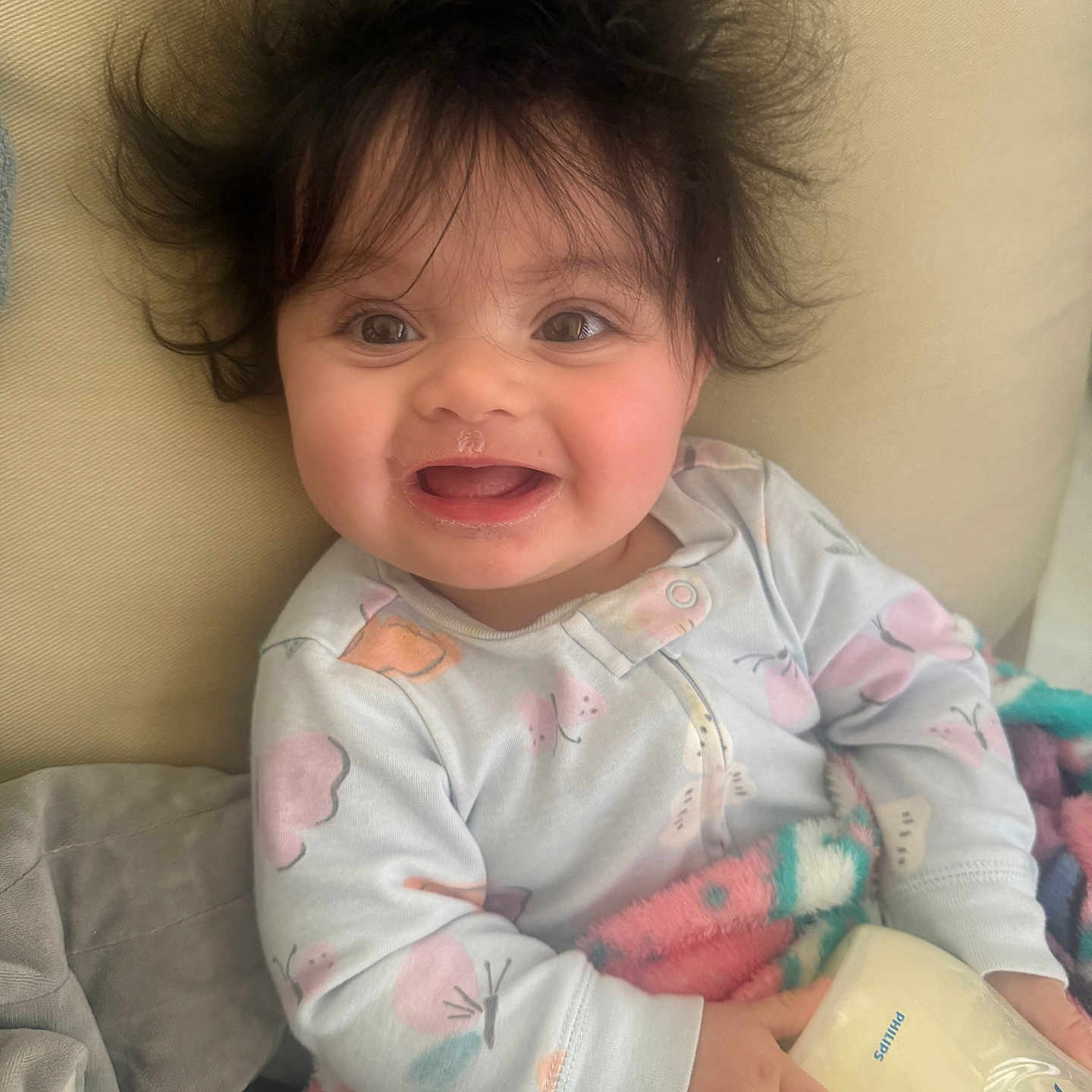 Aviah is registered to the contest to win money with this photo: baby, blanket, child, clothing, cozy, cute, face, hair, happy, home, indoor, infant, joyful, milk_bottle, person, portrait, sitting, smile, soft, young