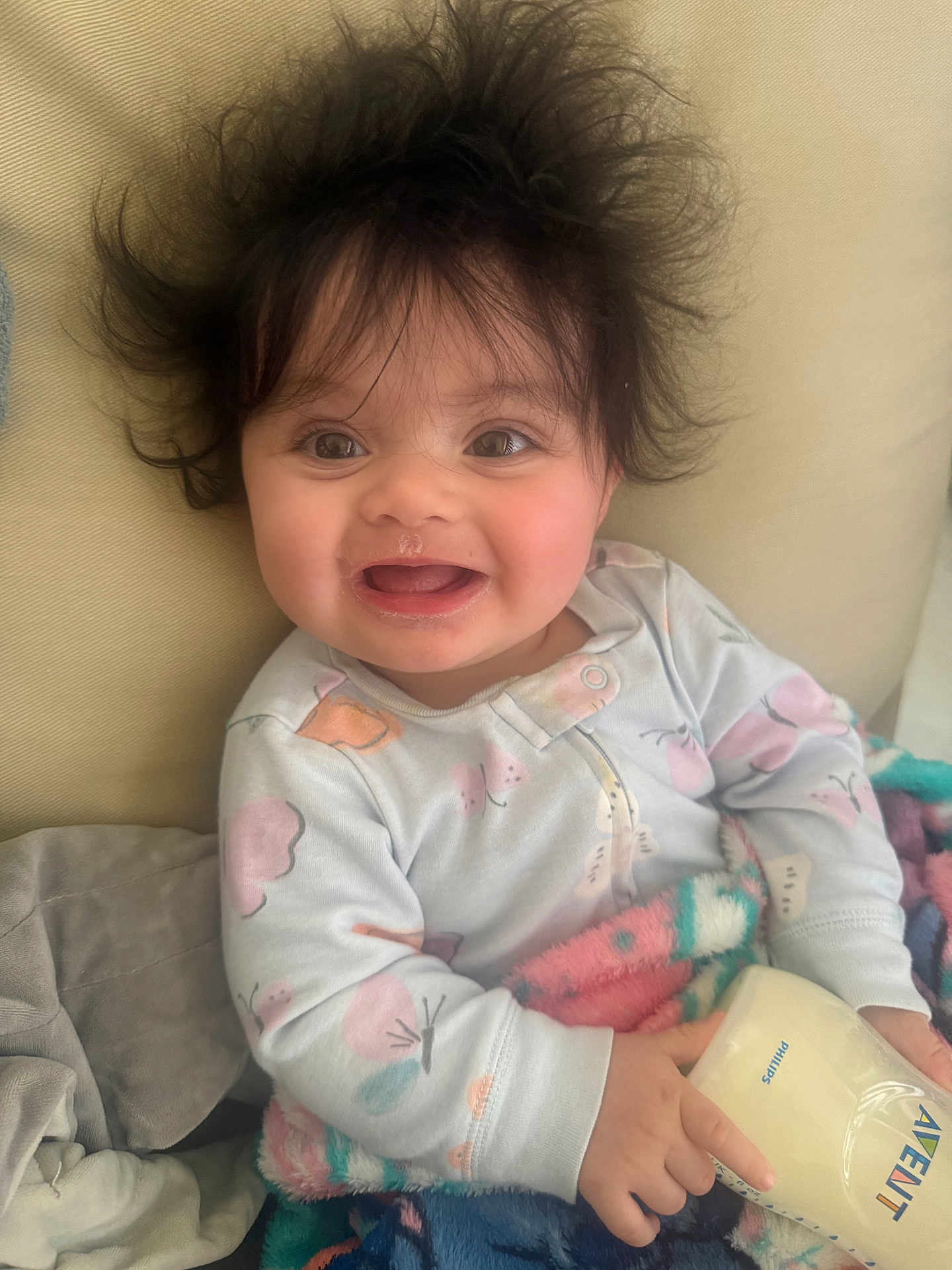 Aviah is registered to the contest to win money with this photo: baby, child, smile, milk_bottle, blanket, hair, happy, indoor, clothing, person, face, cute, infant, cozy, sitting, home, portrait, soft, young, joyful