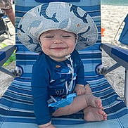 Hayes is registered to the contest to win money with this photo: baby, beach, blue_chair, child, cute, happy, ocean, outdoor, relaxed, sand, seaside, smiling, striped, summer, sun_hat, sun_protection, swimsuit, toddler, vacation, whale_pattern