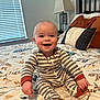 Hayes is registered to the contest to win money with this photo: baby, child, smiling, striped_pajamas, bed, bedspread, pillow, lamp, indoor, happy, sitting, infant, cute, cozy, person, home, nursery, furniture, blanket, portrait