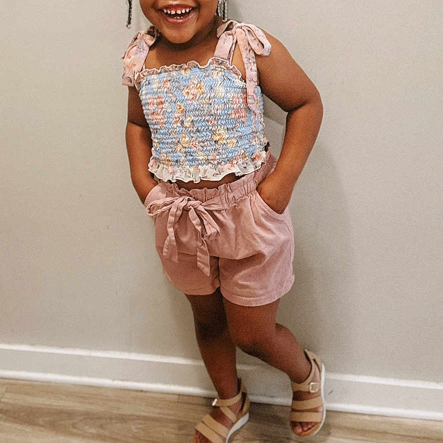 Alyssa Nevaeh is registered to the contest to win money with this photo: bow, braids, child, clothing, cute, fashion, floor, footwear, girl, happy, indoor, person, portrait, pose, sandals, shorts, smiling, standing, top, wall