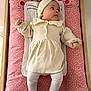 Mia participe au concours pour gagner de l'argent avec cette photo : baby, infant, child, cream_dress, headband, pink_cushion, changing_pad, wooden_frame, baby_clothing, knitted, soft_texture, lying_down, cute, indoor, child_care, face, legs, hands, looking_away, cozy