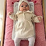 baby, infant, child, changing_pad, pink, cream_clothing, headband, knitted, lying_down, cute, indoors, wooden_furniture, patterned_fabric, tights, small_hands, wide_eyes, portrait, soft_lighting, cozy, adorable