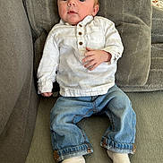 Mattéo participe au concours pour gagner de l'argent avec cette photo : baby, infant, child, white_shirt, blue_jeans, socks, couch, gray_couch, soft_fabric, indoor, portrait, casual_clothing, relaxed, seated, young_child, face, hand, feet, comfort, home