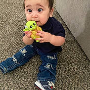 Sky is registered to the contest to win money with this photo: toddler, child, baby_yoda_toy, carpet, jeans, ripped_jeans, sneakers, navy_shirt, indoor, curious_expression, sitting, toy, couch, carpet_floor, person, clothing, hand, footwear, young_child, playful