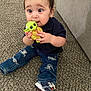 toddler, child, baby_yoda_toy, carpet, jeans, ripped_jeans, sneakers, navy_shirt, indoor, curious_expression, sitting, toy, couch, carpet_floor, person, clothing, hand, footwear, young_child, playful