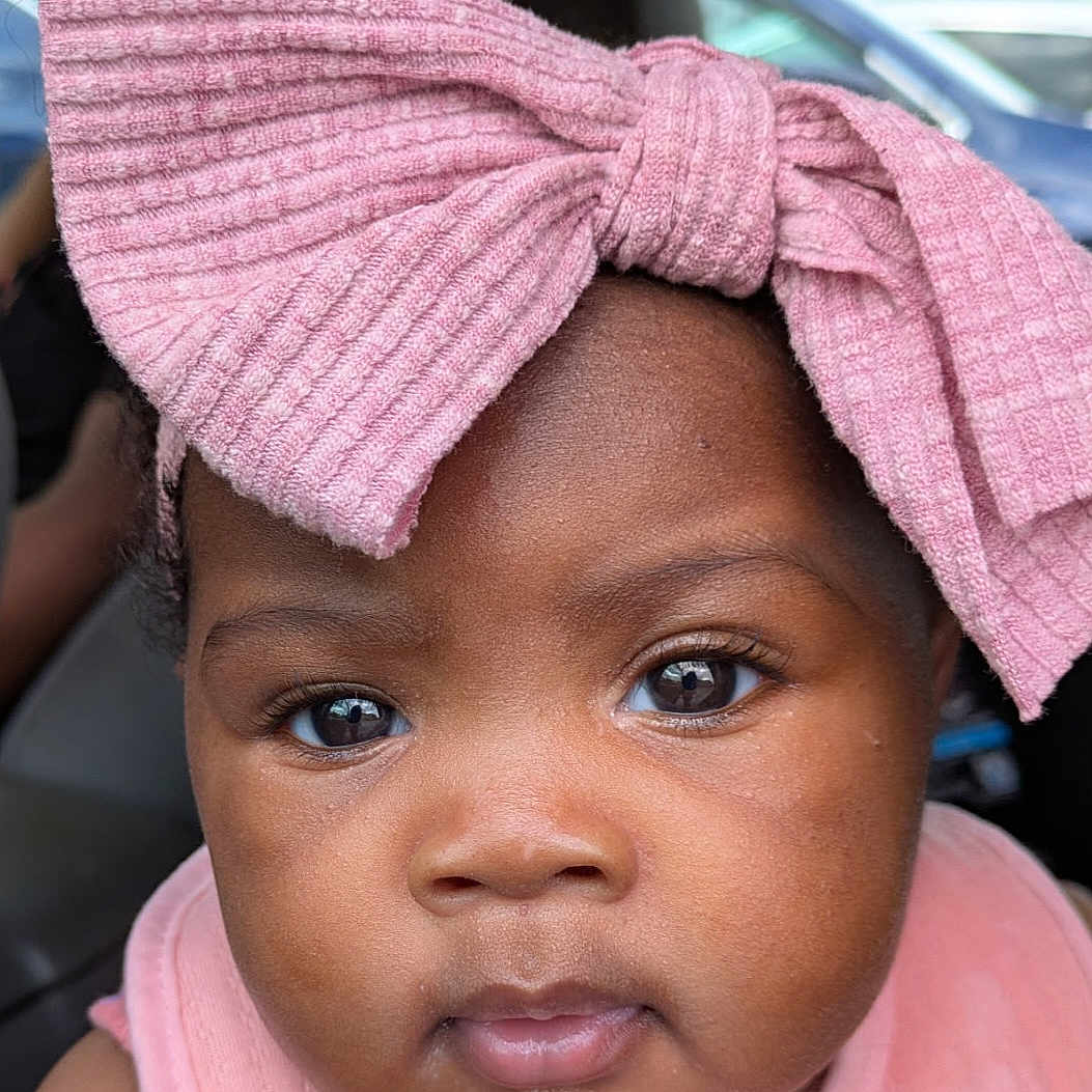Michela is registered to the contest to win money with this photo: accessories, baby, bodypart, bonnet, cap, car, clothing, face, happy, hat, head, headband, person, photography, portrait, purple, smile, transportation, turban, vehicle