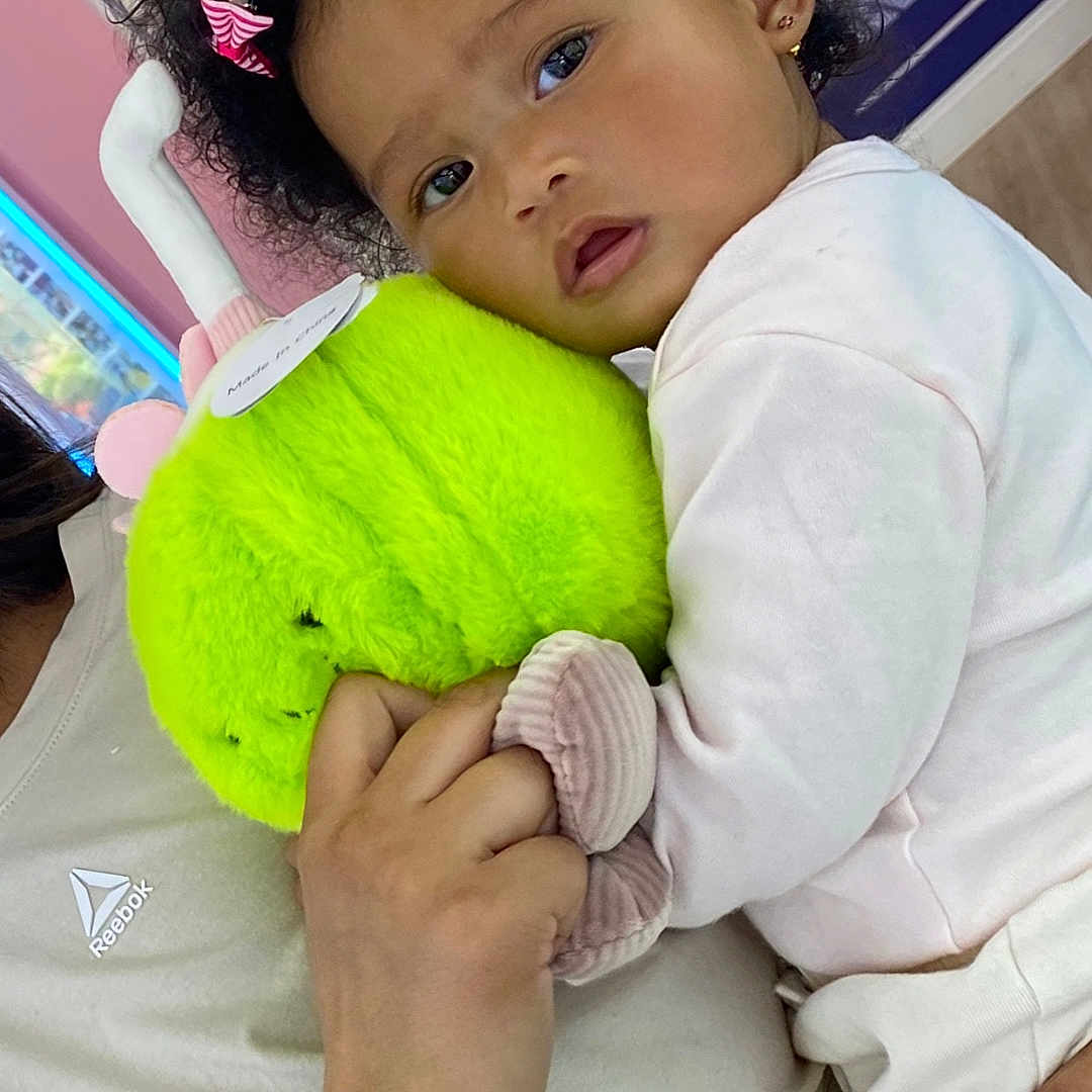 Myliah is registered to the contest to win money with this photo: toddler, child, plush_toy, curly_hair, pink_hair_clip, tattoo, adult, hand, white_clothing, indoor, colorful_background, cartoon, holding, face, expression, cute, cuddling, soft_toy, person, recreation