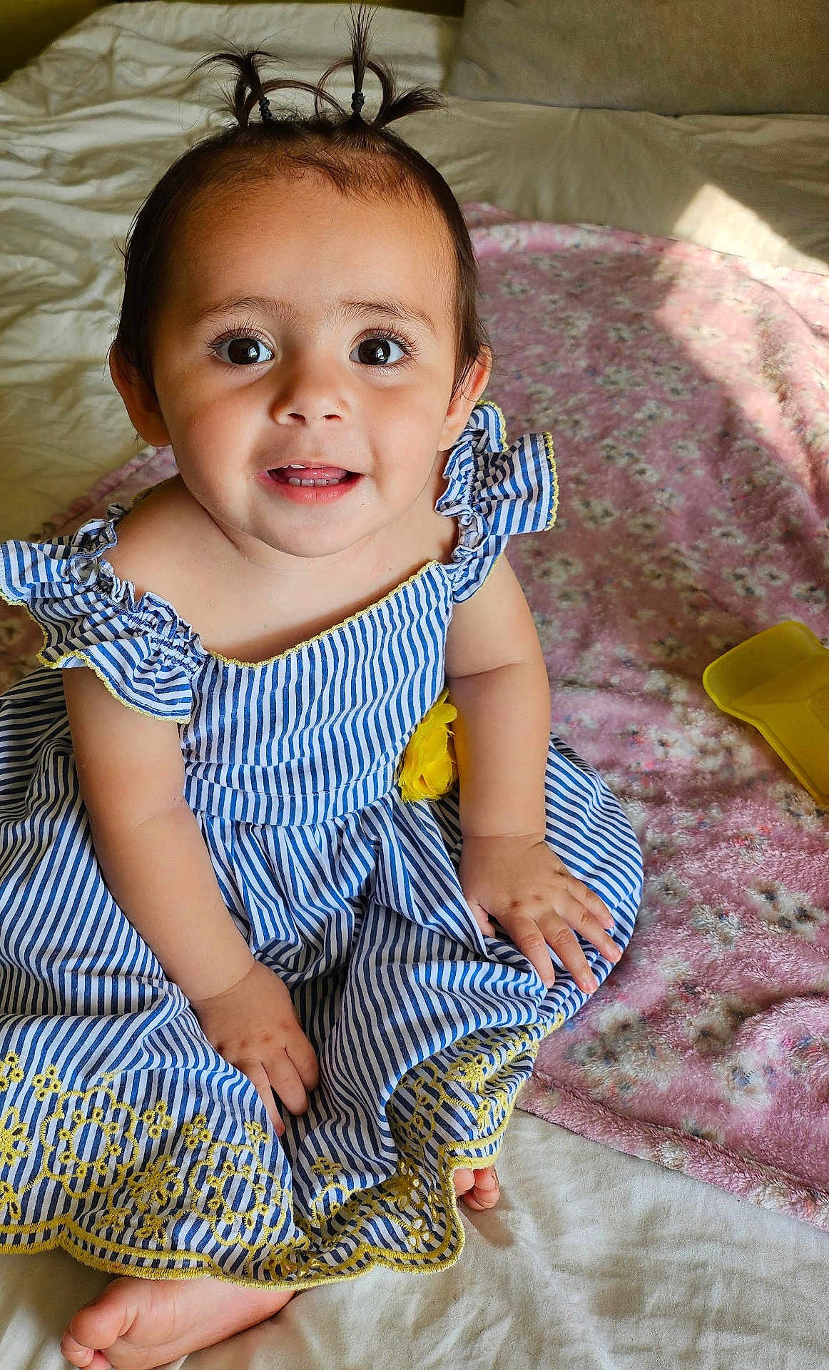 Amelia joined the competition — help win amazing prizes! toddler, child, baby, smiling, blue_dress, striped_dress, pigtails, bed, blanket, yellow_flower, toy_shovel, happy, indoors, portrait, cute, small_hands, bare_feet, soft_light, curly_hair, playtime