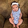 baby, infant, smiling, headband, blue_clothing, onesie, couch, brown_cushion, happy, sitting, cute, child, portrait, indoors, relaxed, skin, furniture, young_child, person, face