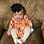 baby, child, smiling, bow, headband, orange_outfit, halloween_theme, ghost_print, pumpkin_print, white_tights, knit, couch, brown_couch, indoor, person, infant, cute, happy, sitting, cozy