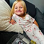 child, toddler, smile, pajamas, ballerina, couch, pillow, blanket, grapes, plastic_container, indoor, cozy, happy, blond_hair, face, person, relaxing, furniture, casual, cute