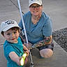 adult, cap, child, concrete, crocs, daylight, family, fun, glasses, hat, lightsaber, outdoor, person, play, shorts, sidewalk, smile, tattoo, toy, tshirt