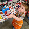 apron, boy, child, clothing, colorful, craft, floor, gift_cards, happy, holding, indoor, playful, project, retail, shoes, short_hair, smiling, store, toddler, young