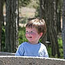 Dean is registered to the contest to win money with this photo: background, boy, casual_clothing, child, cute, daylight, face, greenery, happy, light_blue_shirt, nature, outdoor, playful, portrait, short_hair, smiling, stone_wall, sunlight, trees, young